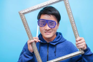 man with funny glasses holding a frame to his face unny wig and a big bow tie in the picture fun team building activity