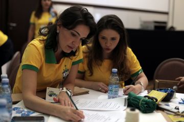 Two women sat at a table with yellow and green shirts on discussing tactics in Catalyst team building activity Goall!!