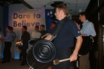 Two men having fun, playing instruments made from recycled materials in Catalyst team building activity Street Beat