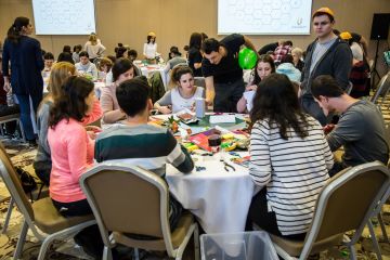 People sat at tables in conference round smiling and laughing playing Catalyst team building activity Bean Around the World 